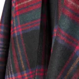 Poncho abierto con diseño de cuadros escoceses en tonos rojo, verde y negro, con terminaciones de flecos en el ruedo.