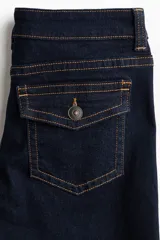 Jean de denim elástico azul oscuro, de tiro bajo, tiro ajustado desde la cintura hasta el muslo y corte acampanado desde la rodilla hacia el bajo. Cuenta con bolsillos delanteros y traseros, cierre frontal con botón y costuras en contraste de color naranja.