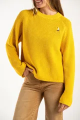 Sweater de punto en color amarillo, con diseño oversize, cuello redondo y manga larga. Presenta un pequeño bordado de un velero en la parte superior del pecho.