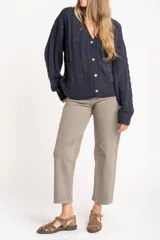 Cardigan de punto texturado con diseño de ochos, color azul marino, con escote en V, cierre frontal con botones dorados y mangas largas con puños acanalados.