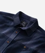 Camisa de franela a cuadros en tonos de azul marino y gris oscuro, con corte regular, manga larga, cuello camisero, cierre frontal de botones y un bolsillo en el pecho.