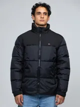 Campera puffer Tommy Hilfiger de color negro, con diseño acolchado, cuello alto y cierre frontal de cremallera. Cuenta con bolsillos laterales con cierre, el logo de la marca bordado en el pecho y un parche con el logo en la manga.