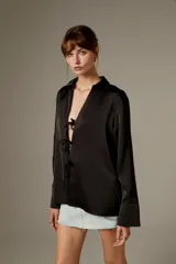 Blusa negra de poliéster, con cuello camisero, mangas largas y cierre frontal mediante tiras para anudar.
