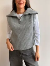 Chaleco de punto acanalado en color gris, con cuello alto y cierre frontal parcial tipo medio cierre. Presenta un diseño sin mangas con corte recto y acabado en tejido de punto de textura marcada.