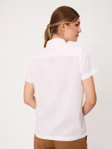 Camisa de manga corta color beige, confeccionada en mezcla de algodón y lino, con cuello camisero, cierre frontal de botones y dos bolsillos aplicados en el pecho.