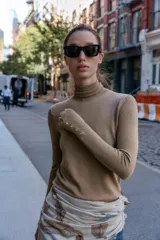 Jersey de punto negro con cuello alto y manga larga, con detalle de botones metálicos dorados en los puños.