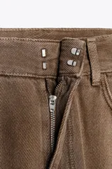 Pantalón de jean color marrón, de tiro alto, corte wide leg y relaxed fit. Cuenta con bolsillos delanteros y traseros, trabillas en la cintura, cierre frontal con cremallera, botón interior y gancho metálico.