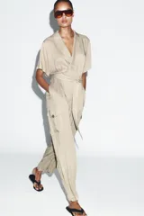 Mono largo de cuello solapa y escote en pico cruzado, con mangas cortas. Presenta bolsillos laterales de plastrón con solapa y botones, y un cinturón del mismo tejido para ajustar en la cintura. Cierre frontal con cremallera y botón interior.