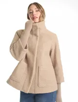 Tapado de tejido boucle color beige con silueta evasé y largo a la cadera. Presenta cuello alto envolvente, cierre frontal con botones a presión ocultos y bolsillos delanteros de gran tamaño. Incluye mangas 3/4 con puños de tejido rib integrados que se extienden hasta las muñecas.