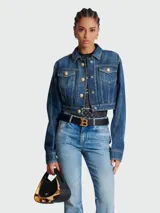 Chaqueta de jean corta azul con efecto desgastado, cuello clásico, cierre frontal con botones dorados y bolsillos con solapa en el pecho.