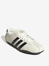 Zapatillas Adidas Tokyo de cuero color crema con detalles en negro, incluyendo las tres tiras laterales y la suela.