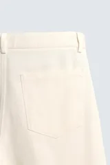 Bermuda de algodón color beige claro, de corte relajado y largo hasta la rodilla. Presenta cierre frontal con cremallera y botón, bolsillos delanteros y bolsillo cerillero, además de bolsillos traseros de plastrón.