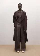 Chaqueta larga tipo gabardina color marrón oscuro, de diseño recto, con solapas amplias y cinturón ajustable del mismo tejido.