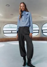 Blusa de color celeste con cuello alto y detalle de fular integrado para anudar. Presenta mangas largas con puños abotonados y un diseño de corte recto.