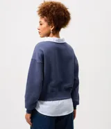 Buzo azul de corte amplio confeccionado en mezcla de algodón y poliéster, con diseño superpuesto que incluye cuello clásico y dobladillo en tono contrastante simulando una camisa por debajo.