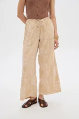 Pantalón ancho de poliéster color beige con diseño bordado floral en hilo blanco, cintura elastizada con cordón ajustable.