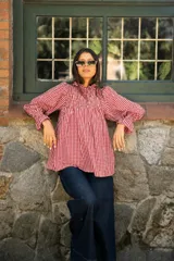 Blusa de algodón con estampado vichy en color rojo y blanco, con diseño de frunces en el pecho, cuello alto con volados y mangas largas amplias con puños elásticos.