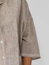 Camisa de corte oversize y diseño holgado, con cuello clásico, cierre frontal de botones y mangas tres cuartos.