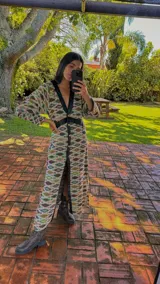 Vestido largo tipo abrigo con estampado geométrico multicolor, cuello en V y solapas de cuero sintético negro. Cierre frontal con botones dorados y detalles de cuero sintético negro en la cintura. Mangas largas y corte holgado.