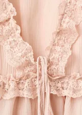 Blusa de viscosa color rosado con escote en V, mangas largas abullonadas con puños ajustables mediante lazos y detalles de puntilla en el escote, bajo y mangas. Presenta un cierre frontal con lazo.