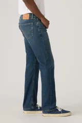 Jeans de mezclilla azul con lavado medio, corte de pierna recta y tiro medio. Presenta cinco bolsillos, cierre frontal con botones y trabillas para cinturón.