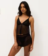 Conjunto de pijama tipo short doll compuesto por una blusa con escote en V y breteles regulables, y un short con cintura elástica. Ambas piezas están confeccionadas en tul transparente con delicados detalles de encaje en el escote y el ruedo.