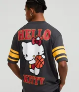 Remera gris oscuro de algodón con corte boxy, cuello redondo y mangas cortas con rayas amarillas. Estampado trasero de Hello Kitty jugando al baloncesto con letras rojas.