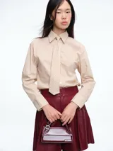 Camisa de corte clásico con estampado de rayas verticales en tonos beige y blanco. Presenta cuello camisero, cierre frontal con botones y corbata integrada del mismo tejido y estampado.
