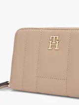 Billetera Tommy Hilfiger color beige con diseño acolchado, cierre de cremallera, múltiples ranuras interiores para tarjetas, compartimento interior para billetes, bolsillo interior con cierre de solapa e insignia del monograma TH dorada en la parte delantera.