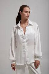 Camisa blanca de mangas largas abullonadas con puños elásticos, cuello clásico y cierre frontal con botones.
