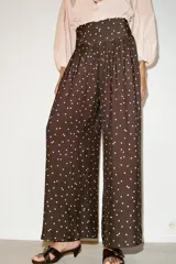 Pantalón de tiro alto con pernera ancha y diseño fluido. Presenta un estampado de lunares blancos sobre fondo marrón y detalle de frunces en la cintura.