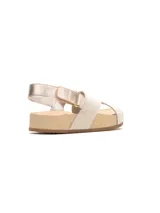 Sandalia plana color beige, con tiras cruzadas en el empeine y tira ajustable con hebilla en el talón. Suela corrida de tono claro con base de goma.