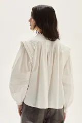 Blusa blanca de algodón con escote alto, detalles de smock y tablitas en el canesú y hombros, y mangas largas abullonadas con puños fruncidos.