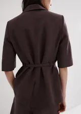Blazer de lino y viscosa color marrón, de diseño recto, cuello en pico con solapa, mangas tres cuartos, dos bolsillos con solapa, cierre frontal con botones y cinturón integrado a juego.