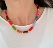 Collar corto tipo gargantilla compuesto por cuentas cilíndricas de colores variados intercaladas con pequeñas esferas doradas.