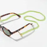 Correa para lentes verde con cuentas acrílicas y terminales de goma transparente. Incluye un dije circular dorado con el logo de la marca grabado.