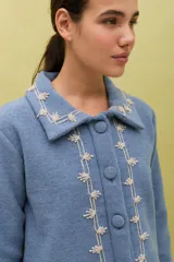 Chaqueta de lana merino hervida en color marrón, con diseño estructurado y cuello amplio. Presenta detalles de bordado artesanal en contraste color mostaza a lo largo del frente, cuello y puños, junto con botones forrados en la misma tela.