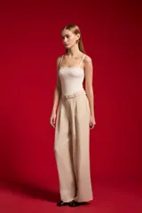 Pantalón ancho de lyocell color beige con pinzas en la parte delantera, tiro alto y un cinturón delgado con hebilla redonda metálica.