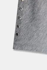 Camiseta de cuello barco y manga larga tipo murciélago, confeccionada en tejido de punto gris melange. Presenta detalle de tachas metálicas a lo largo de los hombros y las mangas.