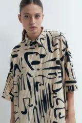 Vestido plisado color beige con estampado abstracto en negro, corte recto, cuello camisero y mangas cortas.