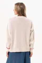 Sweater tejido color crudo con cuello redondo y mangas largas. Presenta dos peces rojos con detalles en azul bordados en el frente. Tiene ribete ondulado rojo en cuello, puños y ruedo.