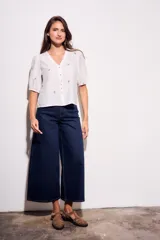 Blusa de viscosa color marrón, con escote en V, mangas cortas abullonadas y cierre frontal con botones. Cuenta con pequeños detalles bordados distribuidos por la prenda.