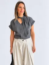 Blusa blanca de rayón y poliéster, con escote en V, detalle de lazo en el cuello, botonadura frontal y mangas cortas con vuelta.