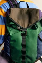 Mochila multibolsillos de diseño colorblock en tonos verde, azul marino, marrón y violeta, con solapa frontal y cierre de hebilla ajustable.