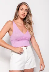 Top tejido color lila, sin mangas, con escote en V profundo y diseño cruzado en frente y espalda. Presenta calados y detalle de punto smock en la parte inferior.