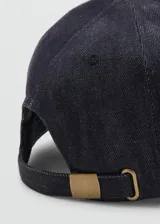 Gorro tipo gorra de visera confeccionado en denim de algodón oscuro, con mensaje bordado y cierre regulable con hebilla metálica.