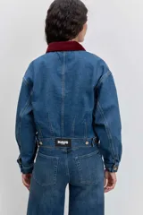 Cazadora de denim azul con corte cropped y diseño de doble botonadura frontal. Presenta un cuello de pana en color bordó y botones metálicos dorados.