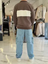 Hoodie de corte clásico con medio cierre y cuello alto, en color marrón con una franja horizontal blanca en el pecho que incluye el logo estampado en negro. Presenta además un pequeño bordado en el hombro izquierdo y puños y cintura elastizados de rib.