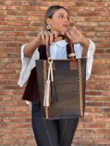 Bolso matero de cuero color chocolate con textura croco, asas cortas y detalle de costuras en los laterales. Incluye un dije con flecos en tonos beige y negro.
