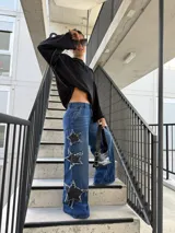 Pantalón jeans azul de corte wide leg, tiro medio y diseño holgado, con grandes aplicaciones de estrellas negras desgastadas en los laterales de las piernas.